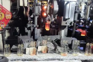 A high-temperature glass bottle molding and conveyor line inside the MYEASY GLASS factory, showing glowing molten jars and automated machinery used in spice jar production.